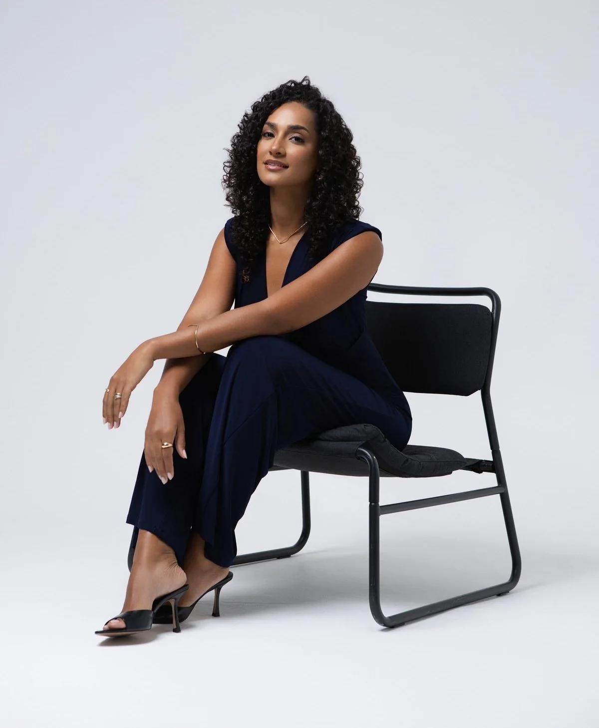 Anna Lobo sentada numa cadeira, vestida de azul escuro, num cenário minimalista cinzento
